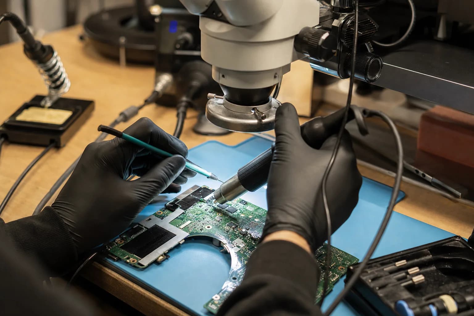 Technician repairing a laptop motherboard under a microscope at an electronics repair bench in Irvine